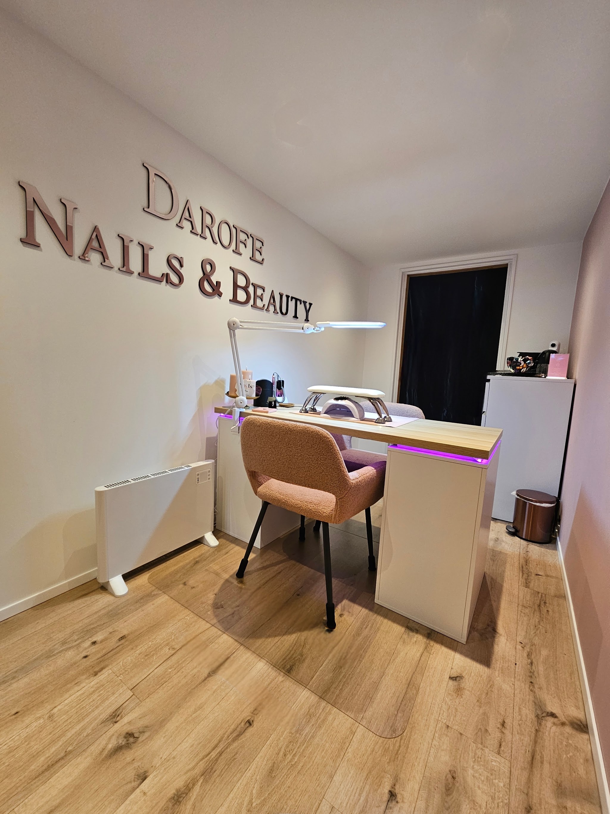 De salon met roze bureau, perzikkleurige stoel, eikenhouten vloer en de letters Darofe Nails & Beauty aan de muur