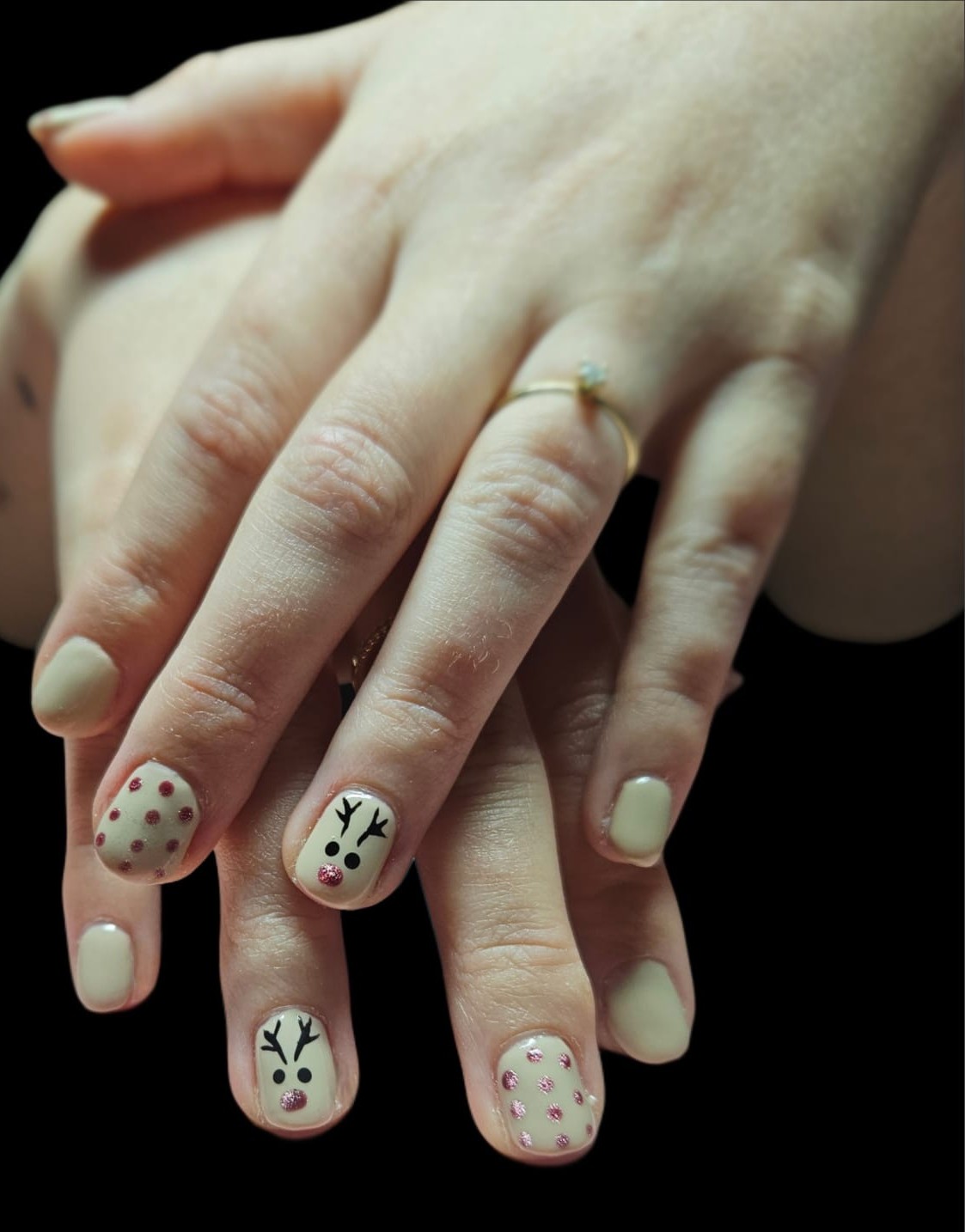 Kerstnagels: lichte nagels met rendieren en roze en rode stippen, op een zwarte achtergrond