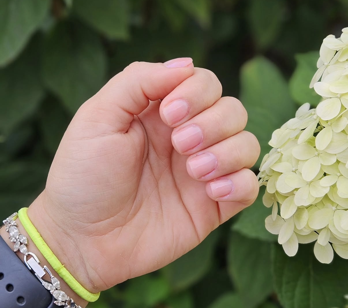 Hand met zacht roze nagels naast witte hortensia's